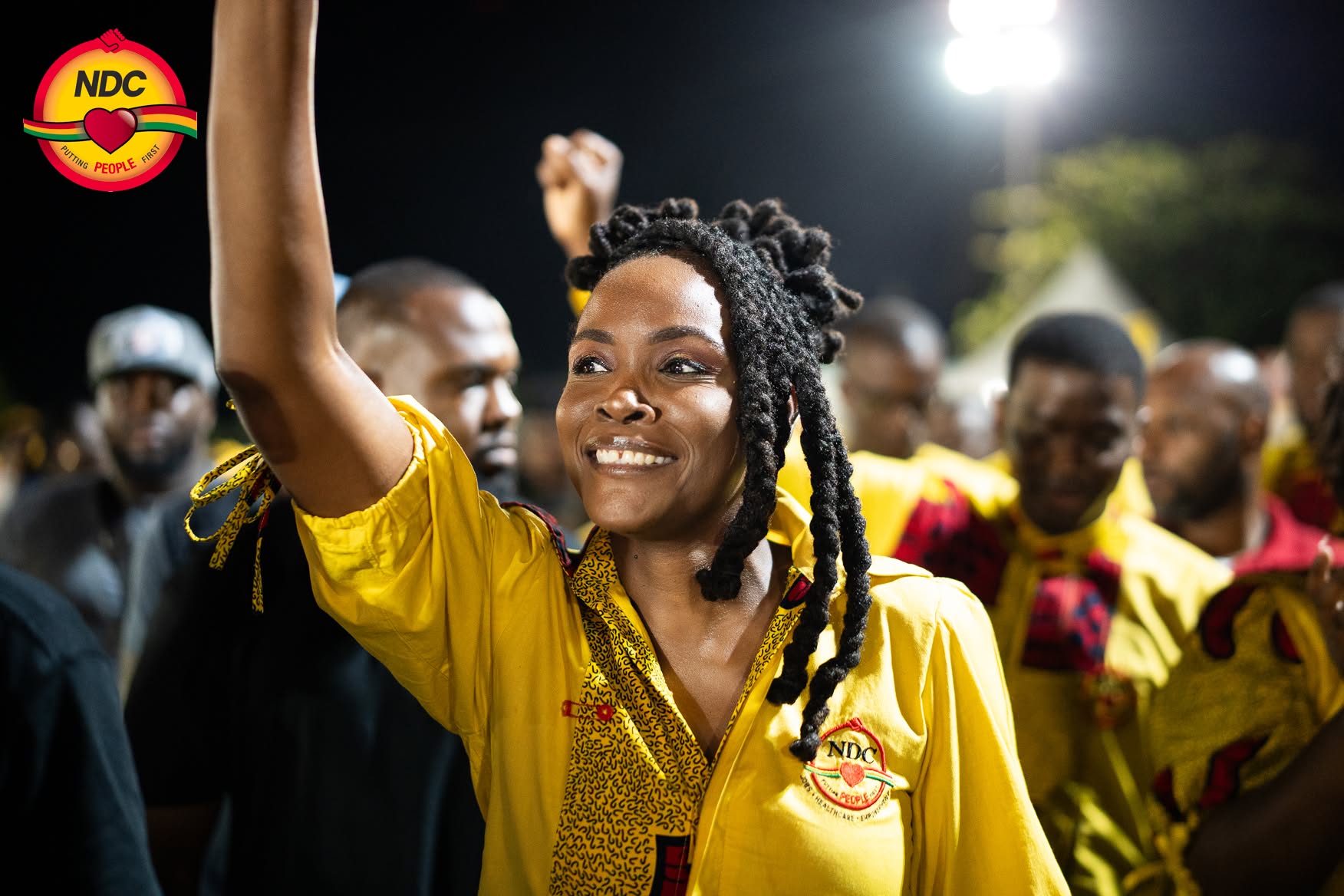 Caris DeGannes smiling with her arm raised among supporters at a night rally